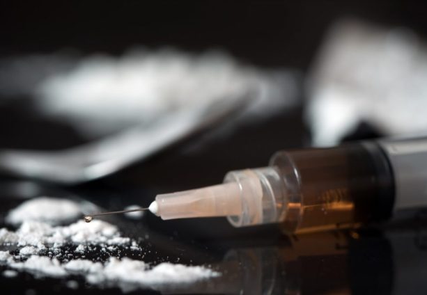 Syringe with drugs laying on a table surrounded by white powder