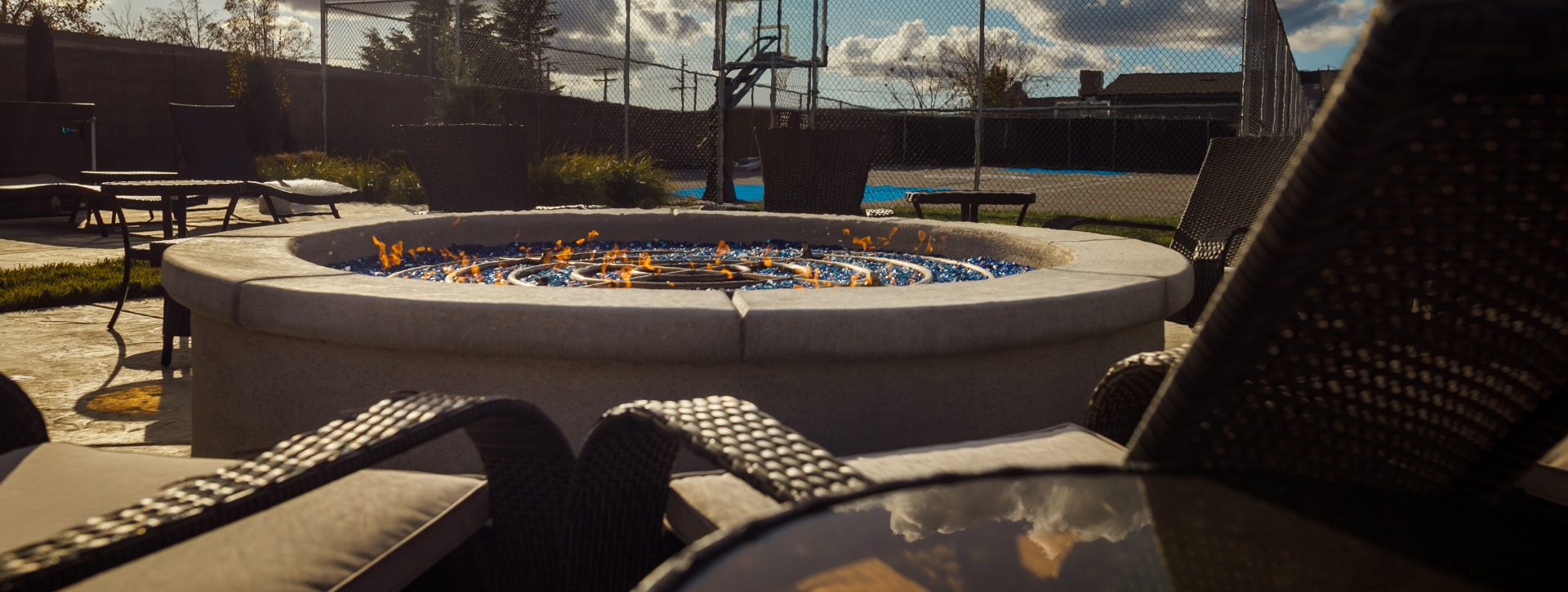 A lit firepit in front of a caged in basketball court