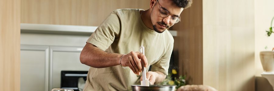 A man cooking. He is holding a rubber spatula and a metal pan.