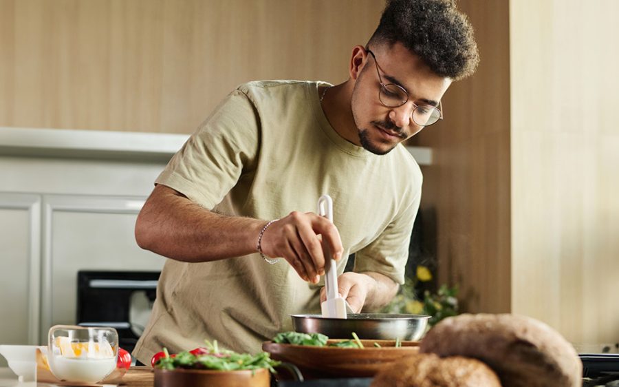 A man cooking. He is holding a rubber spatula and a metal pan.